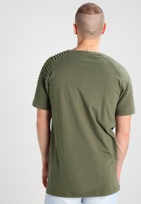 Camiseta verde oliva, de manga corta, con acentos acanalados texturizados en los hombros, fabricada en suave algodón, de corte relajado y con cuello redondo.