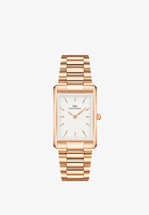 Négyzet alakú, rózsa arany színű óra fehér számlappal, minimalista órajelzőkkel és láncszerű fém karkötővel. A jobb oldalon egy koronával rendelkezik.