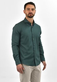 Teal lange mouw shirt met een button-down kraag, zachte stof, slim fit ontwerp en contrasterende knopen. Gecombineerd met lichtbeige broek.