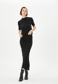 Sort ribbet striktop med korte ærmer, parret med en lang sort bodycon-nederdel. Model iført elegante sorte ankelstøvler.