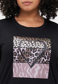 Schwarzes T-Shirt mit einem herzförmigen Design aus verschiedenen Tierdruckmustern in Gold-, Braun- und Rosatönen. Weicher Stoff, runder Ausschnitt.