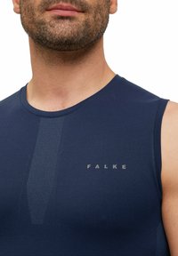 Granatowy damski sportowy top bez rękawów z okrągłym dekoltem, gładką fakturą oraz subtelnym szarym logo "FALKE" na przodzie. Detal bezszwowej konstrukcji.