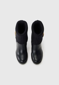 Black leather boots with ribbed knitted tops. Features a round toe and a gold hardware accent on the side. Smooth texture with a flat sole.