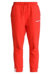 Punaiset collegehousut, jotka on valmistettu pehmeästä kankaasta. Niissä on joustava vyötärönauha, sivutaskut ja valkoinen adidas-logo. Joustavat hihan suut nilkoissa.