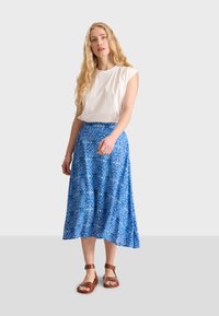 Jupe maxi à motifs bleus, en tissu léger, associée à un top blanc à manches courtes et des sandales à lanières marron.