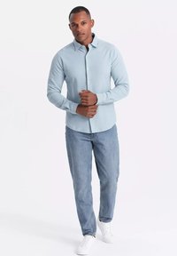 Lichtblauw langemouw shirt met een knoopkraag, gecombineerd met lichte spijkerbroek en witte sneakers. Het shirt heeft een slim fit ontwerp.