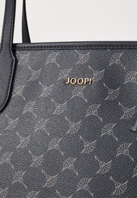 Marineblå tekstureret tote taske med et subtilt lyst mønster, prydet med et guld "JOOP!" logo på forsiden. Inkluderer glatte læderdetaljer.