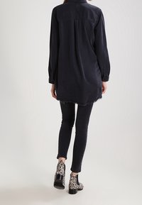 Camicia nera oversize con orlo sfrangiato e maniche lunghe, abbinata a jeans neri slim-fit e stivaletti alla caviglia con stampa leopardata.