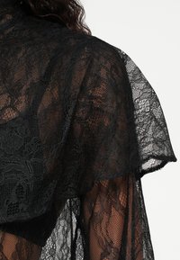 Zwarte kanten kleding met een gestructureerd, gelaagd ontwerp. Bevat ingewikkelde bloemmotieven en een zachte, doorschijnende textuur. Randen zijn gegolfd.