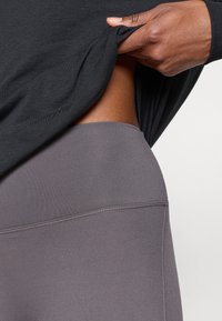 Hallid hallid legginsid sileda tekstuuriga, millel on kõrge vöökoht. Must topp on veidi tõstetud, paljastades vöökohtadel sujuva disaini.