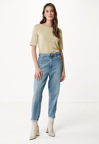 Pruhované žluté a krémové tričko spárované se světle modrými vysokými džíny, nošeno s krémovými kotníkovými botami. Jednoduché pozadí.