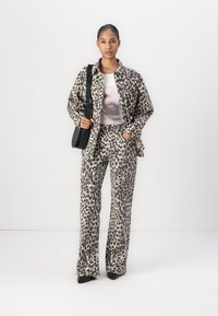 Giacca leopardata e pantaloni abbinati in beige e marrone scuro. Il modello tiene una borsa nera. La t-shirt presenta una grafica ravvicinata delle labbra.