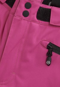 Rosa fiskbensmönstrad tyg med två svarta knappar och ett svart kardborreband. Har en sidoficka med dragkedja och en kontrasterande dragring.