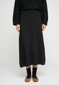 Dolga temno siva pletena krilo z elastičnim pasom in ravnim krojem, kombinirano s črnimi nogavicami in svetlo rjavimi čevlji.