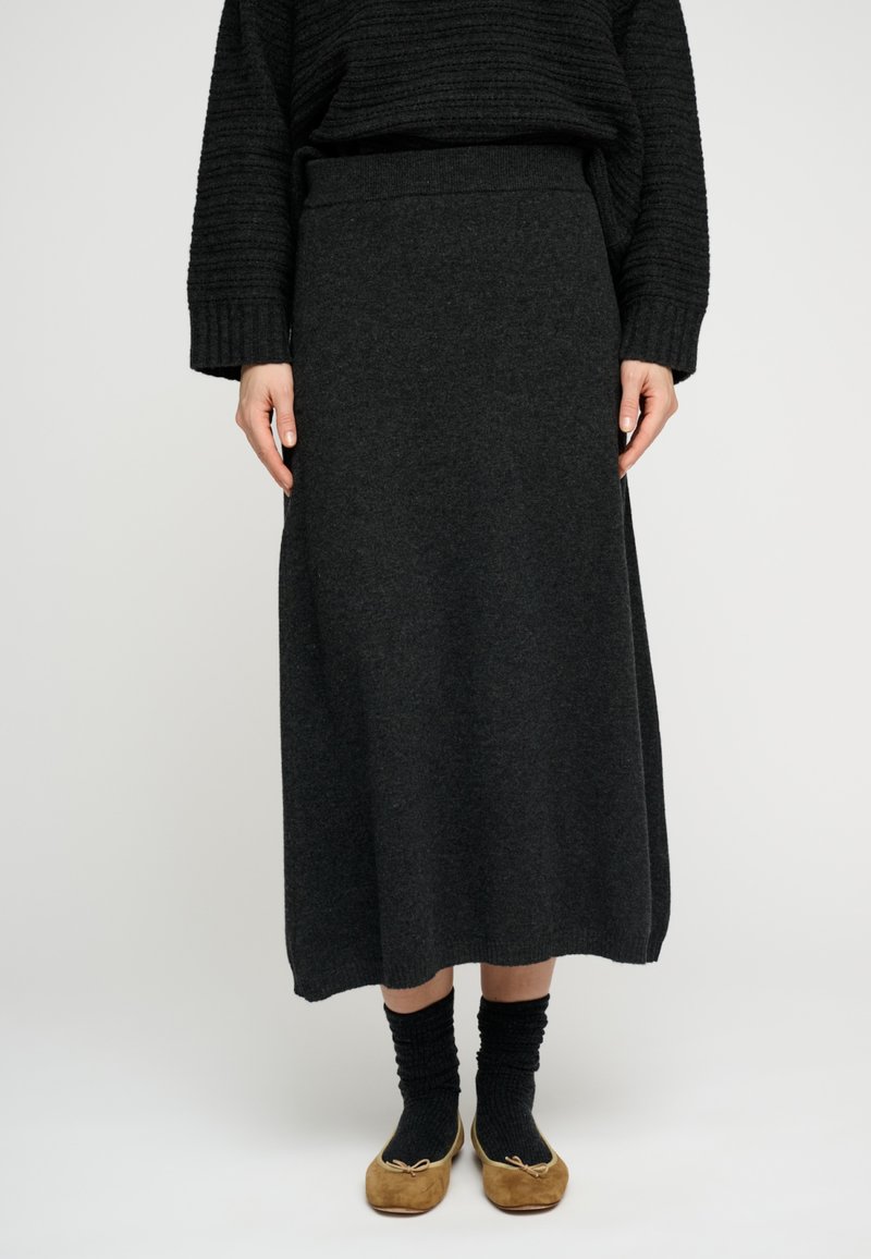 Dolga temno siva pletena krilo z elastičnim pasom in ravnim krojem, kombinirano s črnimi nogavicami in svetlo rjavimi čevlji.