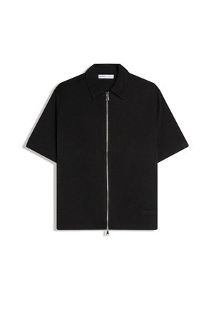 Zwart shirt met korte mouwen, kraag en een zilveren rits die helemaal aan de voorkant loopt, plat gelegd op een witte achtergrond.