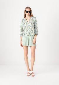 Light floral blouse with puffed sleeves, paired with mint green shorts. The model wears black sunglasses and white heeled sandals.