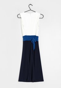 Robe sans manches avec un corsage blanc, une ceinture bleue nouée en nœud, et une jupe fluide bleu marine accrochée à un cintre noir.