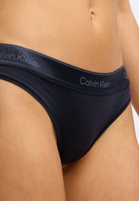 Marineblaue Baumwollslips mit einer glatten Textur und einem charakteristischen Bund, auf dem "Calvin Klein" in passender Farbe eingeprägt ist.