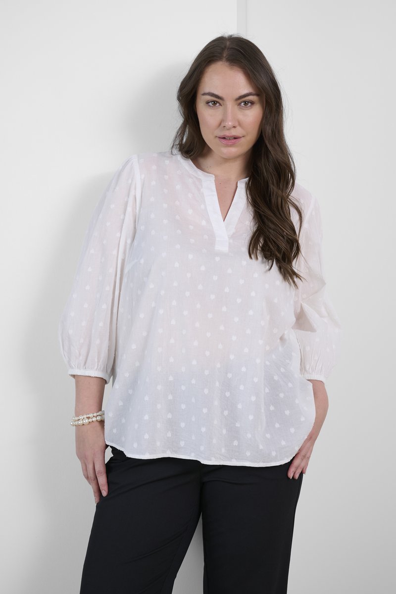 Blouse blanche en tissu léger et transparent, avec un motif de pois subtil, un plastron à demi-boutons et des manches bouffantes.
