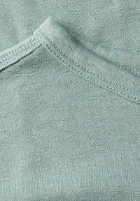 Tissu vert clair, texturé, avec une surface lisse et un col ras du cou ; présente une couture droite le long du col et des épaules.
