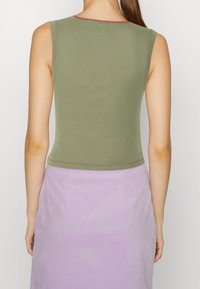 Žena viděná zezadu, oblékající bezramínkový olivově zelený crop top a sukně s vysokým pasem v levandulové barvě, stojící na jednoduchém pozadí.