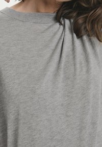 Lys grå t-shirt med rund halsudskæring, blødt bomuldsstoff, og en afslappet pasform, der har subtile folder i stoffet.