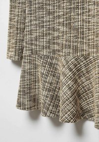 Robe à carreaux marron et crème avec un ourlet évasé. Le tissu texturé présente des motifs de fils variés, créant une apparence superposée.