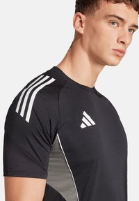 Zwarte sportshirt met korte mouwen, witte schouderstrepen en een slanke, getextureerde grijze zijpaneel met verfijnde patronen.