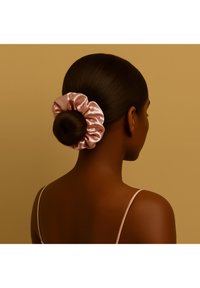 Fermaglio per capelli in raso rosa satinato fissato intorno a uno chignon liscio di colore castano scuro, che mette in risalto una morbida lucentezza e una texture arruffata raccolta su uno sfondo caldo.
