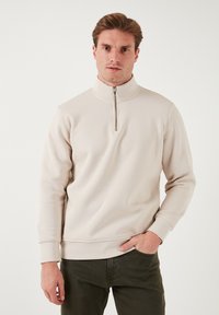 Beige színű, cipzáras nyakú pulóver, puha anyagból készült, hosszú ujjakkal, bordázott mandzsettákkal és sima felülettel. Lazán elegáns dizájn, testhezálló fazonnal.