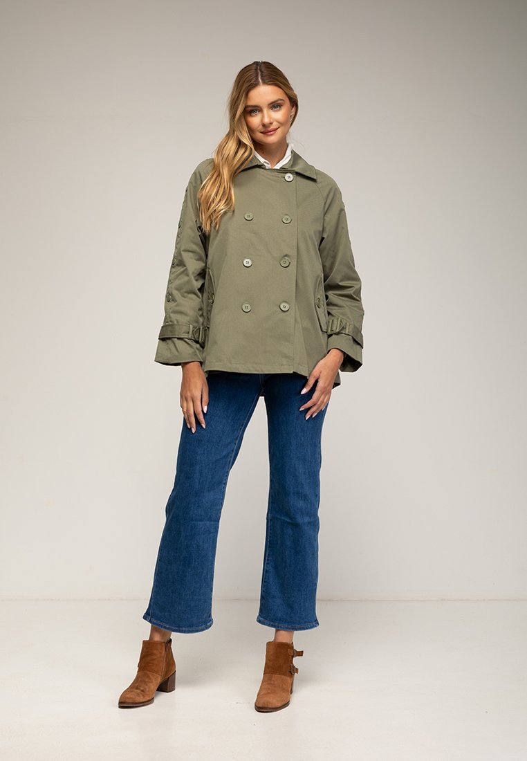 Grüne, doppelt geknöpfte Jacke mit großen Knöpfen, puffärmeligen Ärmeln und seitlichen Taschen, kombiniert mit blauen, ausgestellten Jeans und braunen Stiefeletten.