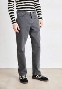 Chino en coton gris avec une coupe droite, dotés de poches frontales, d'un bouton de fermeture, associés à des baskets noir et blanc. Haut à rayures à manches longues.