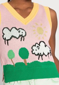 Débardeur en tricot avec un fond rose, des bordures jaunes et des motifs de moutons et de soleil fantaisistes. Des arbres verts sont représentés en bas.