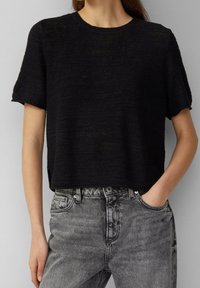 Crop top noir en tricot à manches courtes. Tissu texturé ; assorti à un jean en denim gris délavé taille haute.