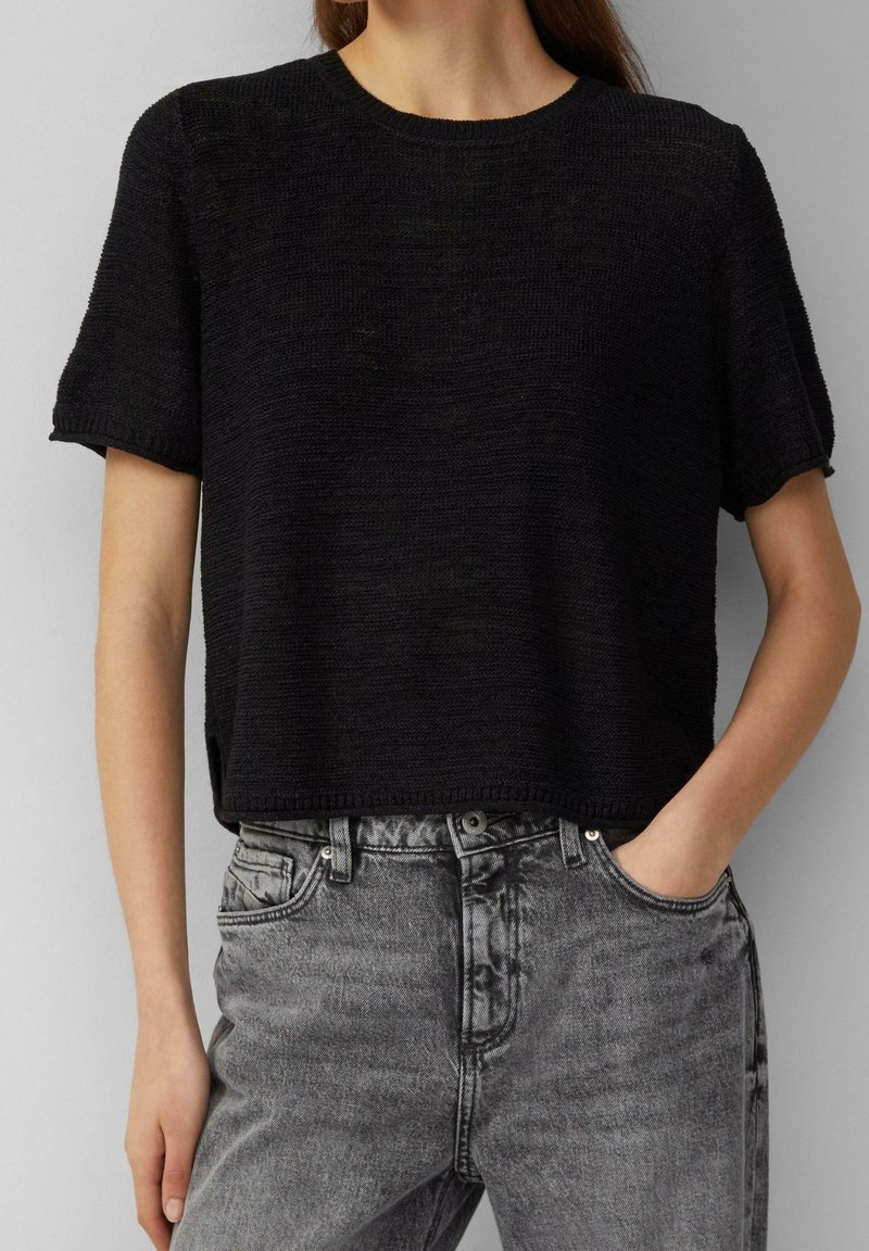 Crop top noir en tricot à manches courtes. Tissu texturé ; assorti à un jean en denim gris délavé taille haute.