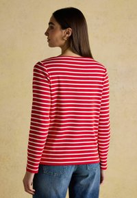 Czerwono-biała w paski koszula z długim rękawem i okrągłym dekoltem, wykonana z miękkiego materiału, w zestawie z niebieskimi dżinsami.