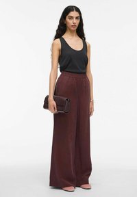 Zwarte mouwloze top, bordeaux brede broek, met een donker bordeaux clutch, en lichtroze schoenen; gladde texturen en een ontspannen pasvorm.