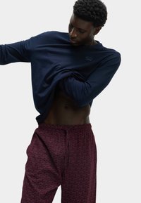 Camisa de manga larga en color navy con cuello redondo y detalle de logo, combinada con pantalones de pijama burdeos con un patrón de animales repetido y cintura elástica.