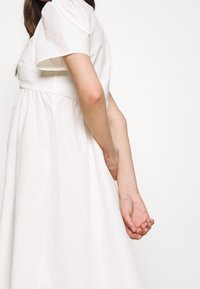 Vit midi-klänning med korta puffärmar, figursydd kropp och en flödande kjol. Tillverkad av mjukt bomullstyg med en mjuk textur.