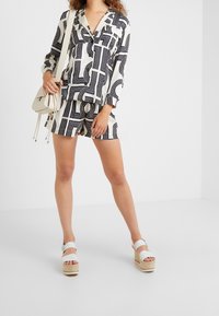 Ensemble deux pièces noir et blanc à motifs comprenant une chemise à col à manches longues et un short assorti, complété par des sandales à plateforme blanches.
