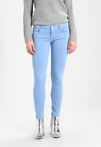 Jeans skinny azul claro en tejido elástico con una textura suave, que cuentan con un diseño clásico de cinco bolsillos y detalles de costura sutiles.