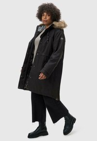 Black parka jacket with a faux fur hood, front pockets, and a floral inner lining, paired with black wide-leg pants and black boots.