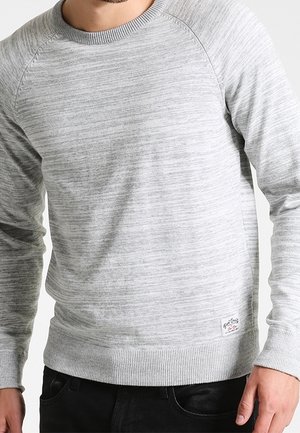 Hellgrauer Langarm-Pullover mit Rundhalsausschnitt und dezenten horizontalen Streifen, getragen von einer Person mit schwarzer Hose, die einen Teil des Oberkörpers zeigt.