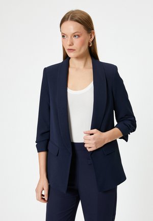 Blazer navy con colletto sciallato, chiusura a un bottone e tasche frontali. Il tessuto ha una finitura liscia e un design strutturato.