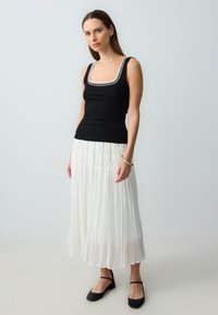 Top in cotone a coste nera con colletto ricamato bianco, abbinato a una gonna maxi plissettata bianca e ballerine nere. Tessuto morbido con vestibilità ampia.