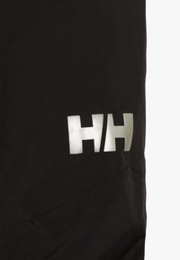 Zwarte buitenkleding met een reflecterend zilver kleurig logo "HH" en subtiele textuur. De stof lijkt glad met minimale stikseldetails.