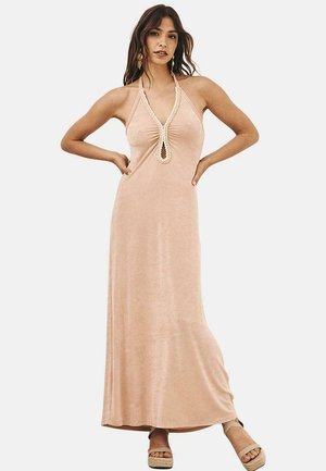 Larga, ligera vestido halter color durazno con un corpiño fruncido y un acento circular. Textura suave, hasta el suelo, combinado con zapatos de plataforma ligeros.