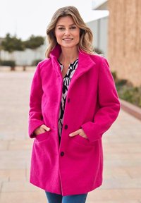 Fuchsia Wolle-Mix Mantel mit Kragen, Frontknöpfen und Seitentaschen. Kombiniert mit einem schwarz-weißen gemusterten Hemd und Jeans.