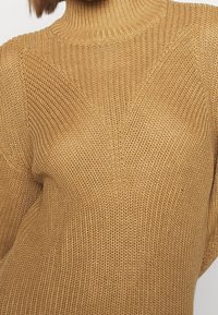 Chunky stickad polokrage i varm karamellfärg. Har ett texturerat mönster, ribbad krage och löst sittande ärmar.